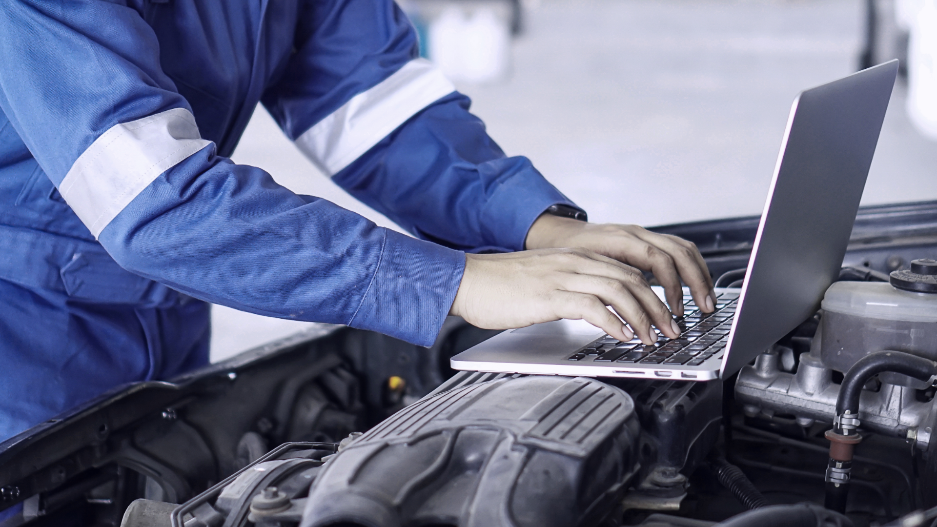 Delphi Technologies expert using a laptop which is resting on top of the exposed engine of a vehicle.