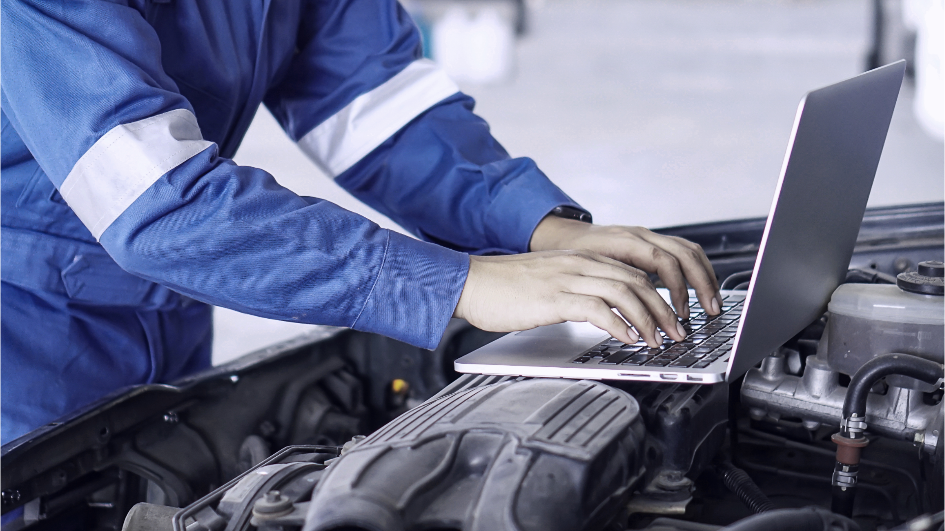 Advance Your Workshop - Top new skills 1920x1080 Delphi Technologies expert using a laptop which is resting on top of the exposed engine of a vehicle.